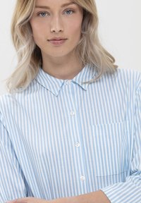 Chemise rayée bleu clair et blanche avec un col, un bouton sur le devant et une poche sur la poitrine. Manches longues avec une texture lisse.