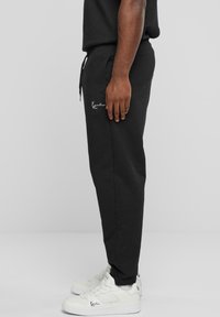 Svart sweatpants med snøring i livet, sidelommer og hvit merkevaredetalj. Kombinert med hvite joggesko med teksturert design.