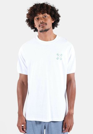 T-shirt en coton blanc à manches courtes, col rond, avec un petit motif floral vert sur le côté gauche de la poitrine. Texture lisse.