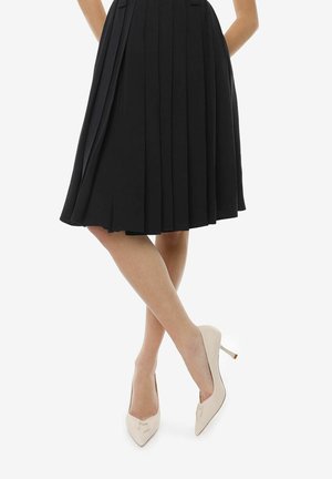 Black pleated skirt with an A-line shape, paired with cream high-heeled shoes featuring a pointed toe and minimal hardware detail.