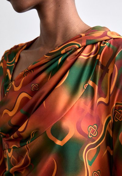 Flowing, orange fabric with green and yellow abstract patterns; features a softly draped neckline and smooth texture.