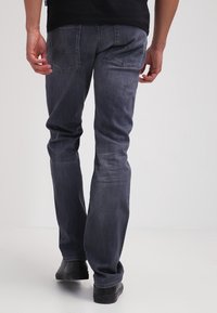 Jeans de mezclilla de un gris oscuro desvaído con un diseño de pierna recta, que cuentan con dos bolsillos traseros y detalles de costura. Combinados con zapatos negros.