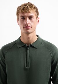 Donkergroene pullovertrui met een kwart-rits halslijn, met een effen textuur en een klassiek kraagontwerp.