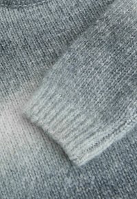 Sweter dzianinowy w gradientowych odcieniach niebieskiego. Posiada ściągacz na rękawach oraz miękką, teksturowaną włóczkę z delikatnym efektem ombre.