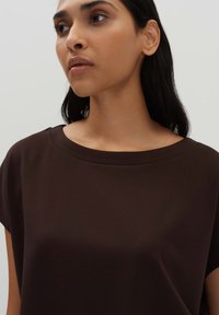 Dunkelbraunes, kurzärmliges Oberteil mit weitem rundem Ausschnitt und weichem, glattem Stoff, das eine lässige Passform und ein minimalistisches Design aufweist.