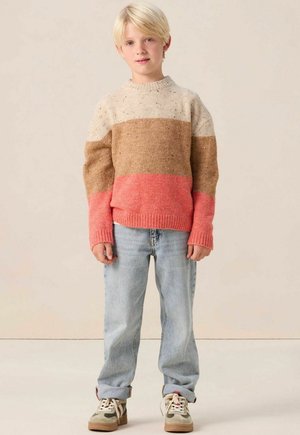 Pull en laine avec des rayures horizontales beige, marron et corail, doté d'un col rond et de poignets côtelés. Porté avec un jean bleu clair et des baskets.
