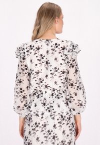 Gennemsigtig bluse med blomstermønster i nuancer af sort og grå. Flæse på skulderen, indsnævret talje og lange puffede ærmer.
