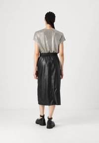 Metalická stříbrná blůza s krátkým rukávem a vertikálními pruhy, spárovaná s midi sukní z černé kůže se strečovým pasem a viditelnými švy.