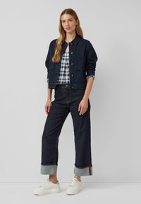 Dunkelblaue Jeansjacke mit einem Kragen, Knopfverschluss und zwei Vordertaschen. Kombiniert mit weiten, dunklen Jeans und weißen Sneakers.