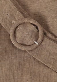 Brązowa tkanina lniana z okrągłym detalem w postaci pierścienia i zapięciami na guziki. Teksturowana powierzchnia, prosty design i neutralna paleta kolorów.