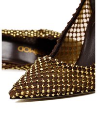 Bruine pointed-toe stiletto schoen met een textuurstof versierd met gouden studs en een gaasontwerp langs de rand, geplaatst op een donkere binnenzool.