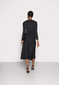 Svart långärmad topp i kombination med en svängande svart midiklänning med åtsittande midja och mjukt, slätt tyg. Buren tillsammans med svarta sandaler med remmar.