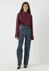 Top burdeos de manga larga con un acabado texturizado, combinado con pantalones de mezclilla azules de cintura alta con un patrón de rayas de cebra y piernas acampanadas.