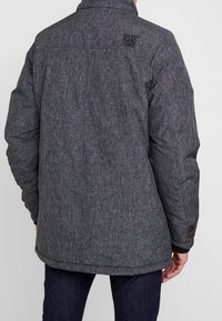Chaquetón gris texturizado con un alto cuello, bordado de la marca en la parte posterior y detalles de botones en los puños.