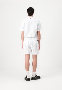 Kortermet skjorte med krave og matchende shorts i hvid med lyseblå lodrette striber. Har elastisk talje og logodetalje.
