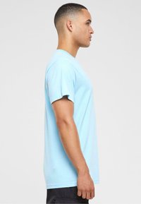 T-shirt en coton bleu clair à manches courtes, encolure ronde et coupe droite, présentée de côté sur un fond neutre.