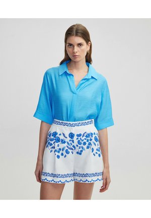 Heldere blauwe korte mouwen shirt met een kraag, gecombineerd met witte shorts met blauwe bloemenborduursels en geprinte accenten aan de zoom.