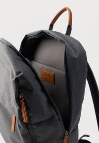 Γκρι υφασμάτινο σακίδιο με καφέ δερμάτινες λεπτομέρειες, κεντρική θήκη με φερμουάρ και πλεγμένο γκρι ιμάντα. Το εσωτερικό διαθέτει λείο ύφασμα και θήκη.