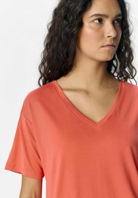 Koralfarvet V-hals t-shirt i blødt, glat stof, med korte ærmer og en afslappet pasform, der viser stikningsdetaljer ved halsudskæringen og kanten.