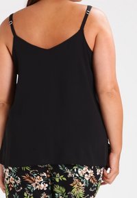 Haut sans manches noir avec un dos en V et des bretelles ajustables ; associé à un pantalon à motifs floraux avec des accents verts et crème.