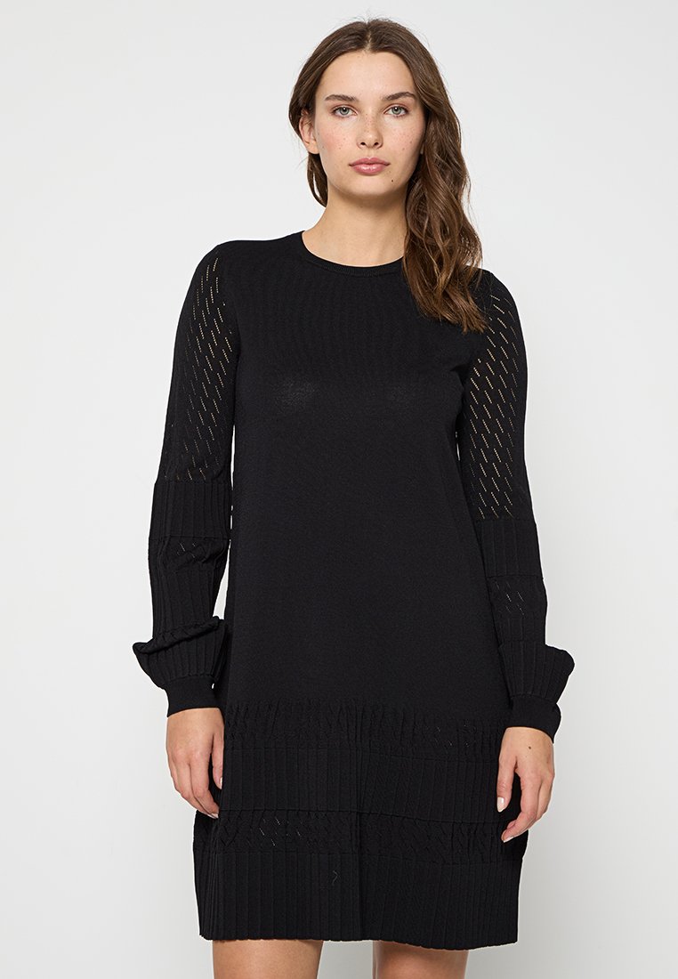 Robe noire en tricot avec un col rond, des manches longues dotées de panneaux en maille et une texture côtelée au niveau de l'ourlet et des manches.