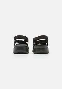 Sandalias negras con tiras entrelazadas y una suela acolchada. El material superior es suave, mientras que la suela presenta un patrón texturizado para mayor agarre.