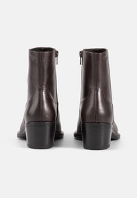 Stivali ankle in pelle marrone con finitura liscia, chiusura con zip e tacco impilato, che mostrano un design snello e dettagli di cucitura minimi.