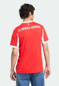Maillot de soccer rouge avec des accents blancs, portant "FC BAYERN MÜNCHEN" au dos. Fabriqué en tissu léger, à manches courtes, coupe décontractée.