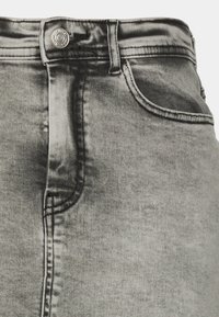 Šedá džínová sukně s hladkou texturou, která má přední kapsu, kovové zapínání na knoflík a jemné vyblednutí pro opotřebovaný vzhled.