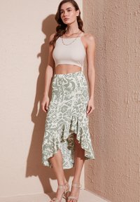 Top cropped bianco abbinato a una gonna verde con motivo e orlo arricciato. L'outfit è completato da sandali con tacco nudo.