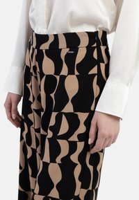 Beige und schwarze, weit geschnittene, gemusterte Hosen mit abstrakten Formen, aus einem weichen Stoff mit glatter Textur und einem seitlichen Reißverschluss.