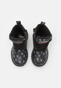 Bottes noires pour enfants avec une finition brillante. Présentent des motifs de cœurs gris clair et des points. Dotées de lacets et de fermetures éclair latérales pour un enfilage facile.