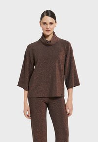 Brauner, glitzernder Strickoberteil mit Schalkragen und drei Viertelarmen, kombiniert mit passenden Hosen. Weiche Textur mit subtilen Glitzerdetails.