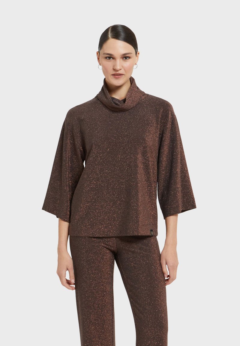 Brauner, glitzernder Strickoberteil mit Schalkragen und drei Viertelarmen, kombiniert mit passenden Hosen. Weiche Textur mit subtilen Glitzerdetails.