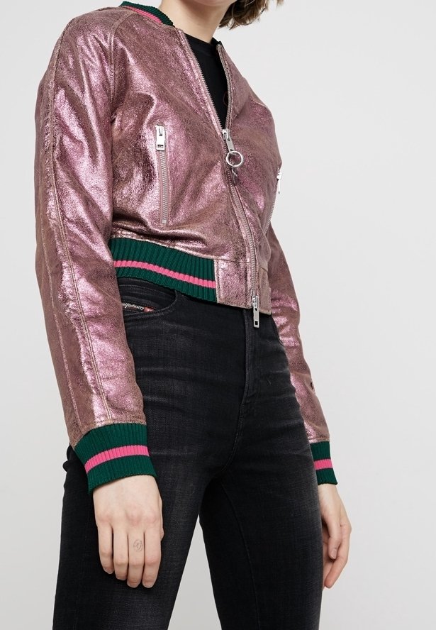 Metaliczna różowa kurtka bomberka z zapięciem na zamek, z zielonymi i różowymi paskami na ściankach oraz bocznymi kieszeniami, zestawiona z czarnymi dżinsami.