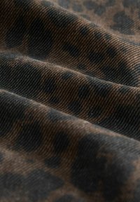 Tissu marron et noir avec un gros plan sur un motif léopard et une texture de tissage diagonale visible.