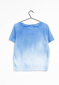 Camisa de manga corta con degradado azul, textura suave, corte relajado, mangas raglán y un parche rectangular en la parte posterior cerca del cuello.