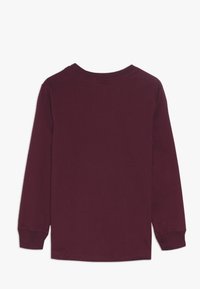 Långärmad skjorta i djup burgund, tillverkad av mjuk bomull. Har rundad hals och ribbade ärmslut, med en enkel och slät yta.