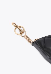 Angolo di una borsa in pelle nera con dettagli in catena d'oro e chiusura, caratterizzata da una texture trapuntata e una finitura liscia.