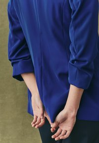 Royal blue blouse with 3/4 sleeves and a relaxed fit. The fabric appears smooth, with a subtle sheen and gentle draping at the back.