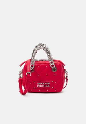 Sac à main matelassé rouge avec poignées en chaîne argentée, détails cloutés, bandoulière réglable et logo "Versace Jeans Couture" sur le devant.
