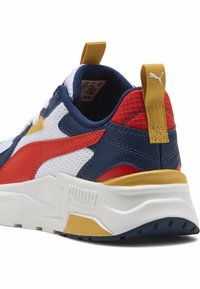 Sportlik spordijalats valgete, tumesiniste ja punaste toonide kombinatsioonis, millel on kollane kand. Sellel on tekstuuriga pind ja silmapaistev Puma logo külgedel.