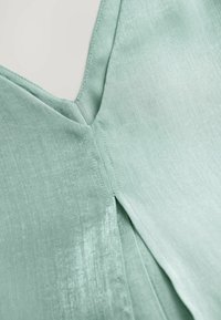 Tessuto verde menta con una consistenza liscia, caratterizzato da un colletto a V e una cucitura laterale con dettaglio a plissettatura.
