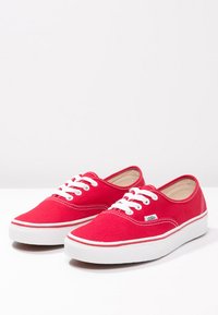 Røde lerrets sneakers med hvite gummisåler, rund tå og detaljer med dobbel søm. Har hvite snørebånd og et logomerke på siden.