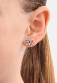 Orecchio con un orecchino a perno a forma di farfalla argentata, con dettagli in smalto rosa e verde, indossato da una persona con capelli castano chiaro.