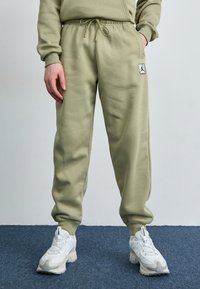 Lyse olivenfarvede joggers lavet af glat stof, med elastisk talje, ribbede manchetter og en logo patch på låret.