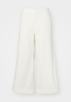 Baltos plačios kelnės, pagamintos iš lengvos medžiagos, turinčios aukštą liemenį ir siuvinėjimo detales, siūlančios laisvą prigludimą ir švarias linijas.