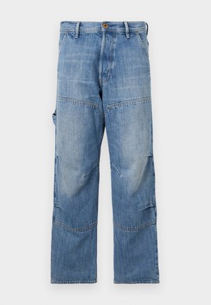 Lyseblå denimbukser med vide ben, slidte områder og patchwork-sømme. Har en frontknap og lynlås lukning med sidelommer.