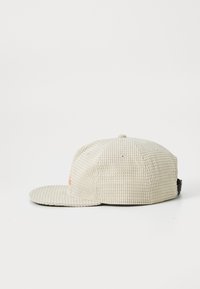 Boné de basebol texturizado em bege com um padrão quadrado de waffle e aba reta, visto de lado sobre um fundo branco.