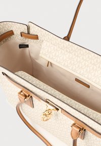 Borsa tote beige con stampa firmata, dettagli in metallo dorato, inserti in pelle liscia, apertura superiore senza chiusura e tasca interna con zip. Interno foderato con texture minimale.